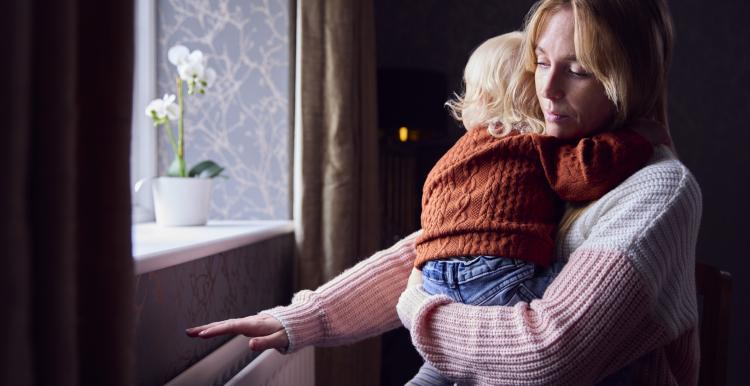 Woman holding a small child with her hand over the heater