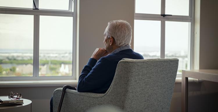 Elderly man sitting in an armchair looking out a window