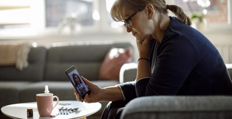 Middle-aged lady with glasses in her home, on a video call with a doctor.