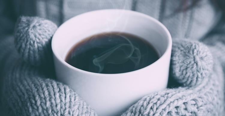 Hands wearing mittens holding a mug of hot drink