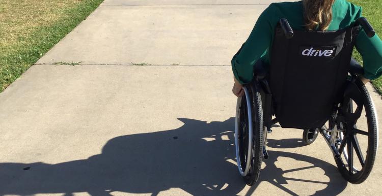 A woman in a wheelchair outside on a path.