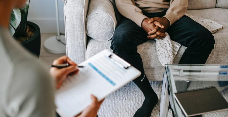 Person taking notes while speaking to somebody seated on a sofa