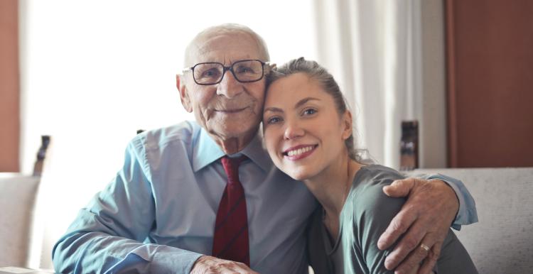 Elderly man hugging a young lady while sitting at a table.