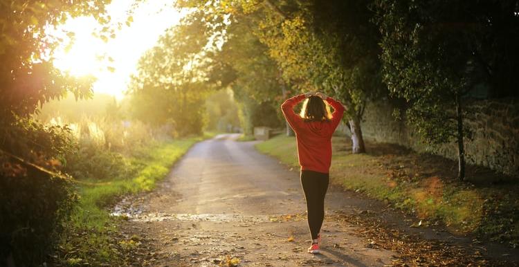 Girl wearing a red jumper walking down a leafy lane with arms outstretched