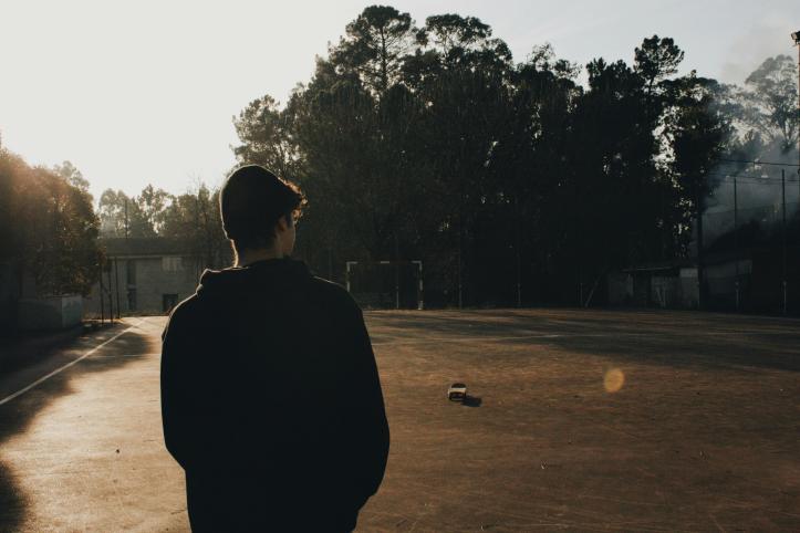 Back view of teenage boy looking at an empty football pitch.