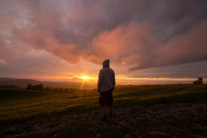 Silhouette of a man in a hooded jacket looking at a sunset