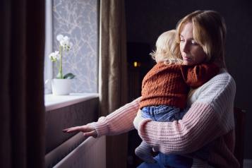 Woman holding a small child with her hand over the heater