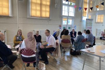 People meeting in a hall sitting in groups having discussions 