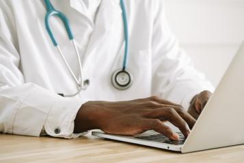 Black doctor typing on a laptop with stethoscope around neck