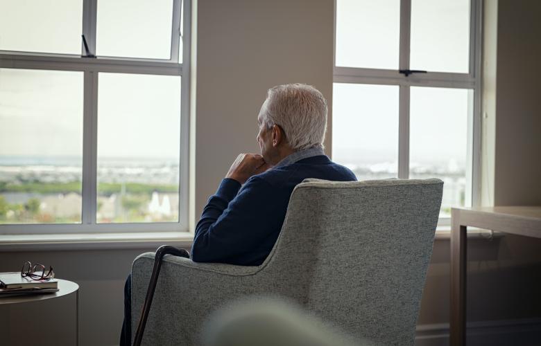 Elderly man sitting in an armchair looking out a window