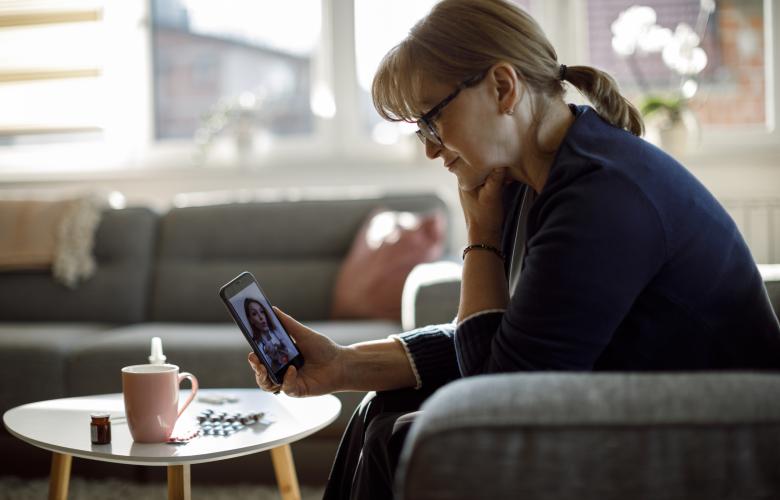 Middle-aged lady with glasses in her home, on a video call with a doctor.