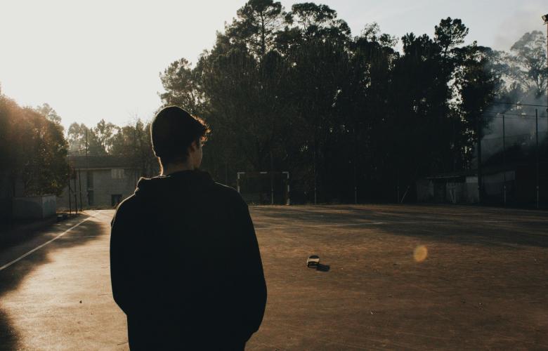 Back view of teenage boy looking at an empty football pitch.